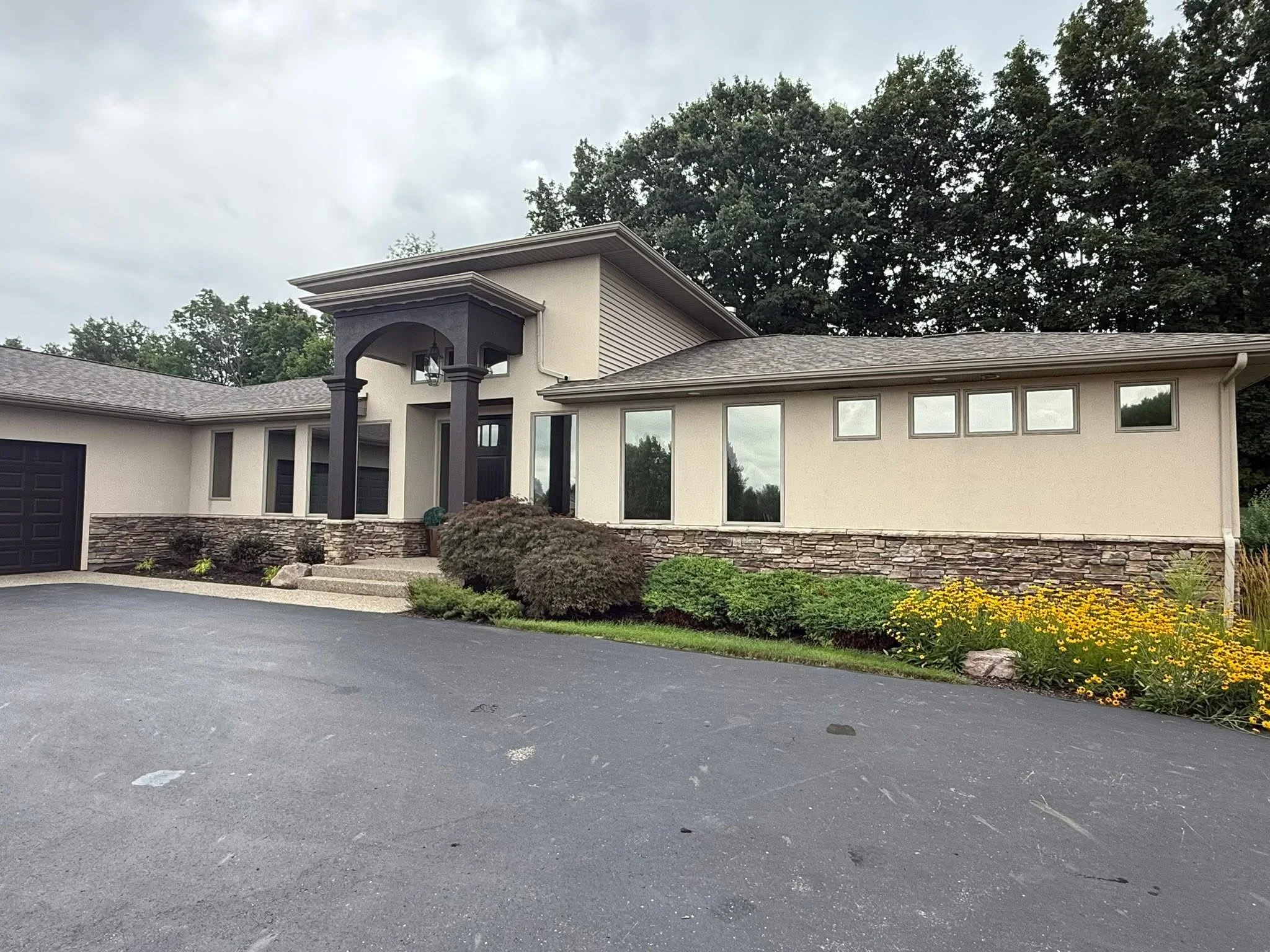 Modern home with large installed windows, stone veneer base, and dark entry portico