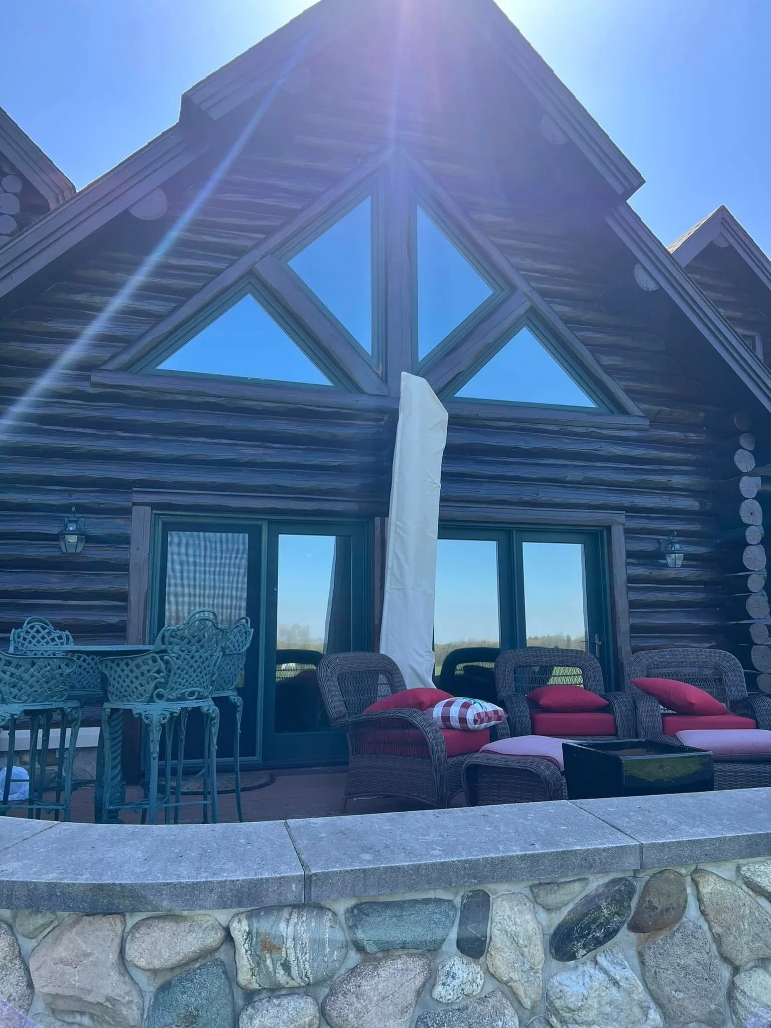 Tinted gable windows on log cabin with stone foundation and patio seating