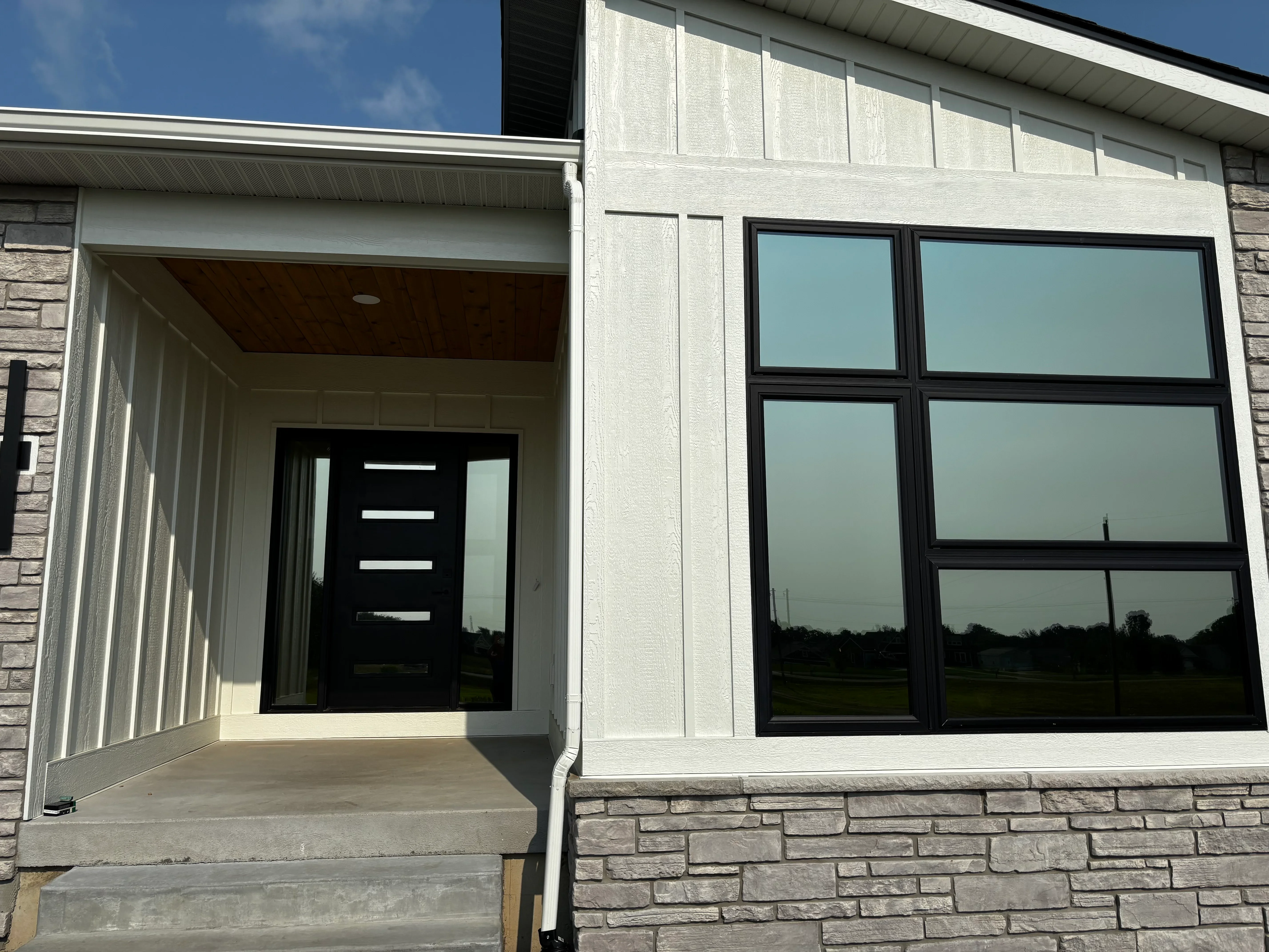 Black-framed windows and door with light blue window tint applied to residential home exterior