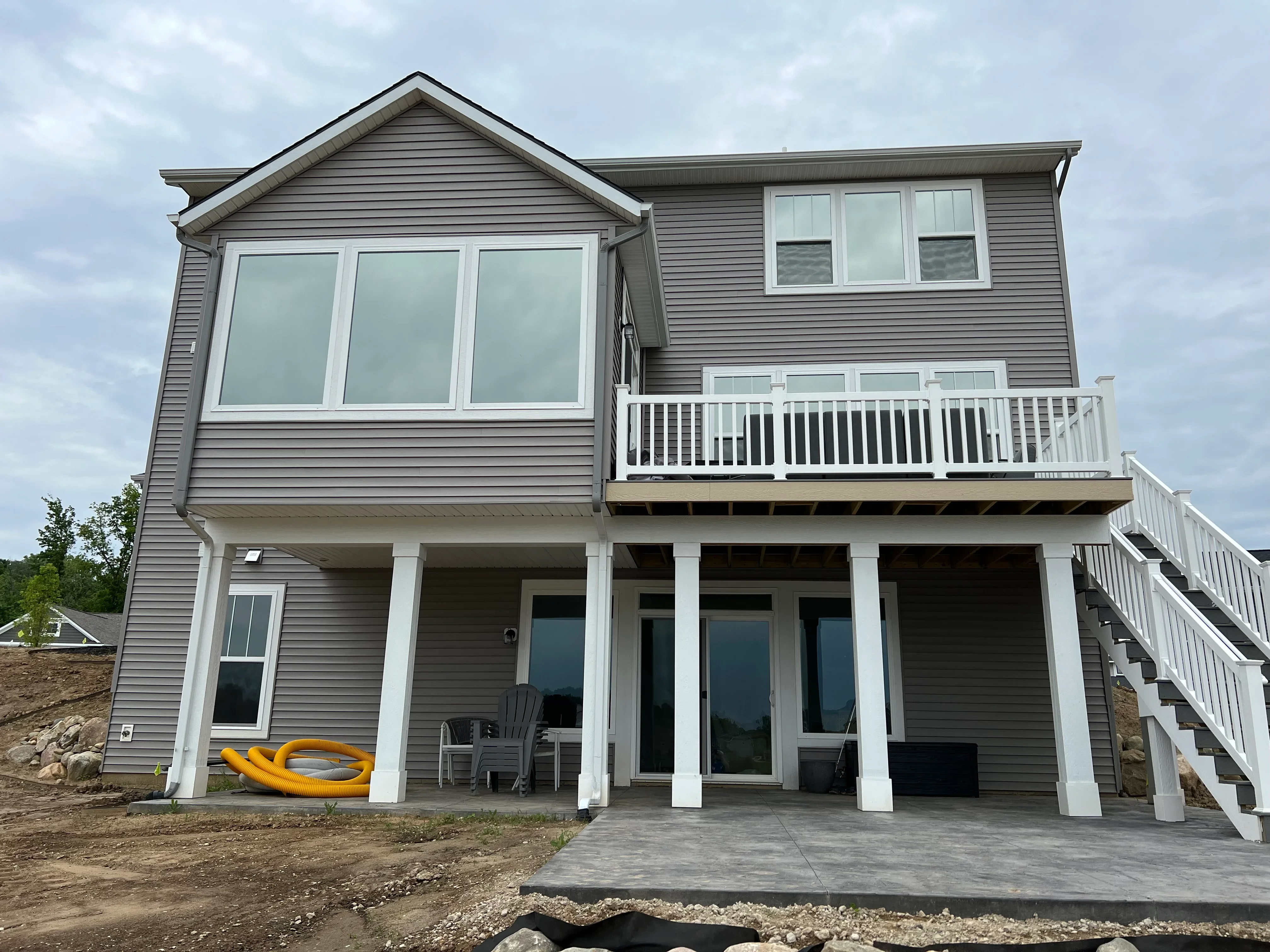 Residential home with tinted windows on gable and main level, white deck railings, concrete patio