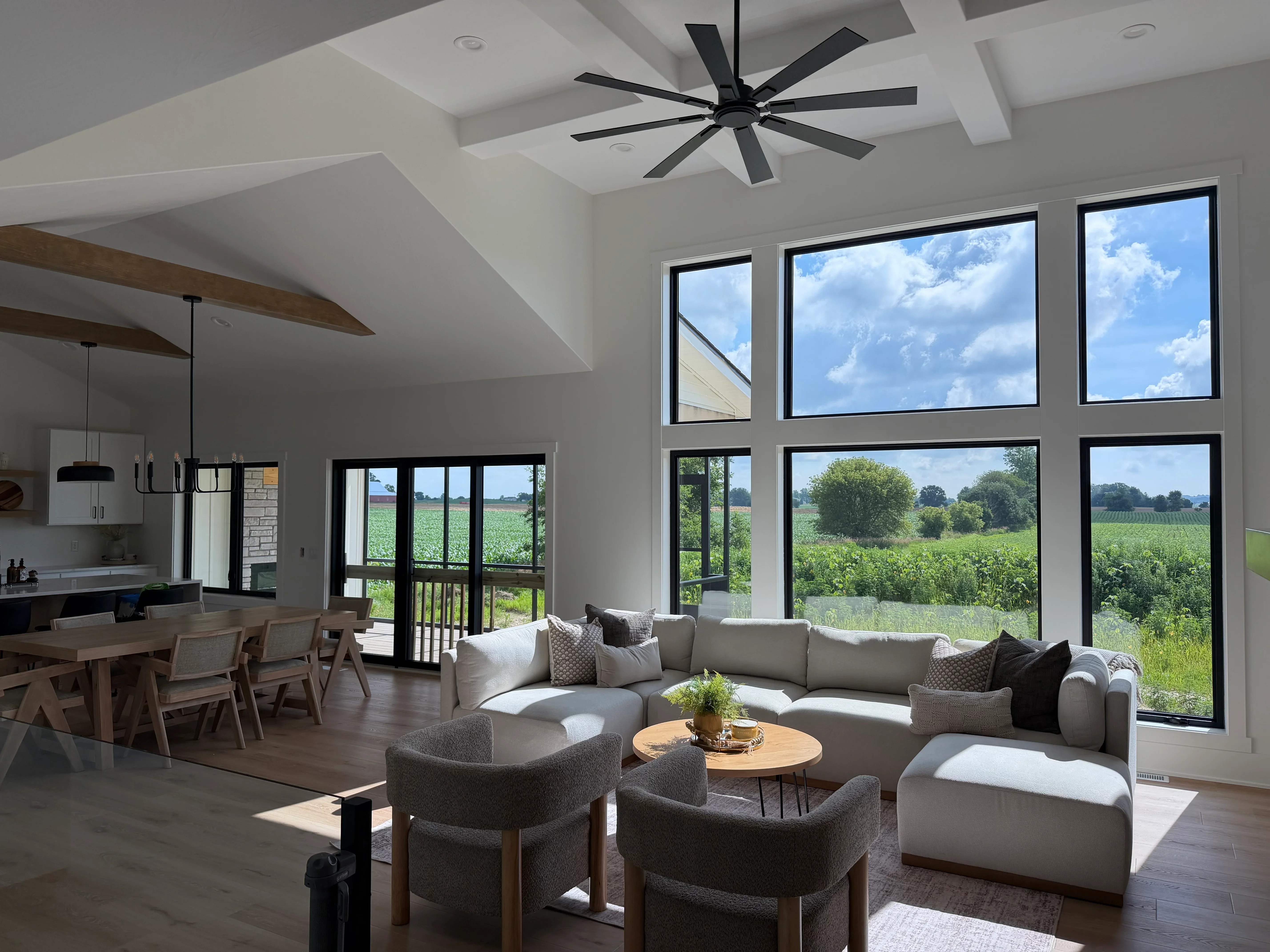Black-framed windows and glass doors in modern great room with white drywall and wood beams
