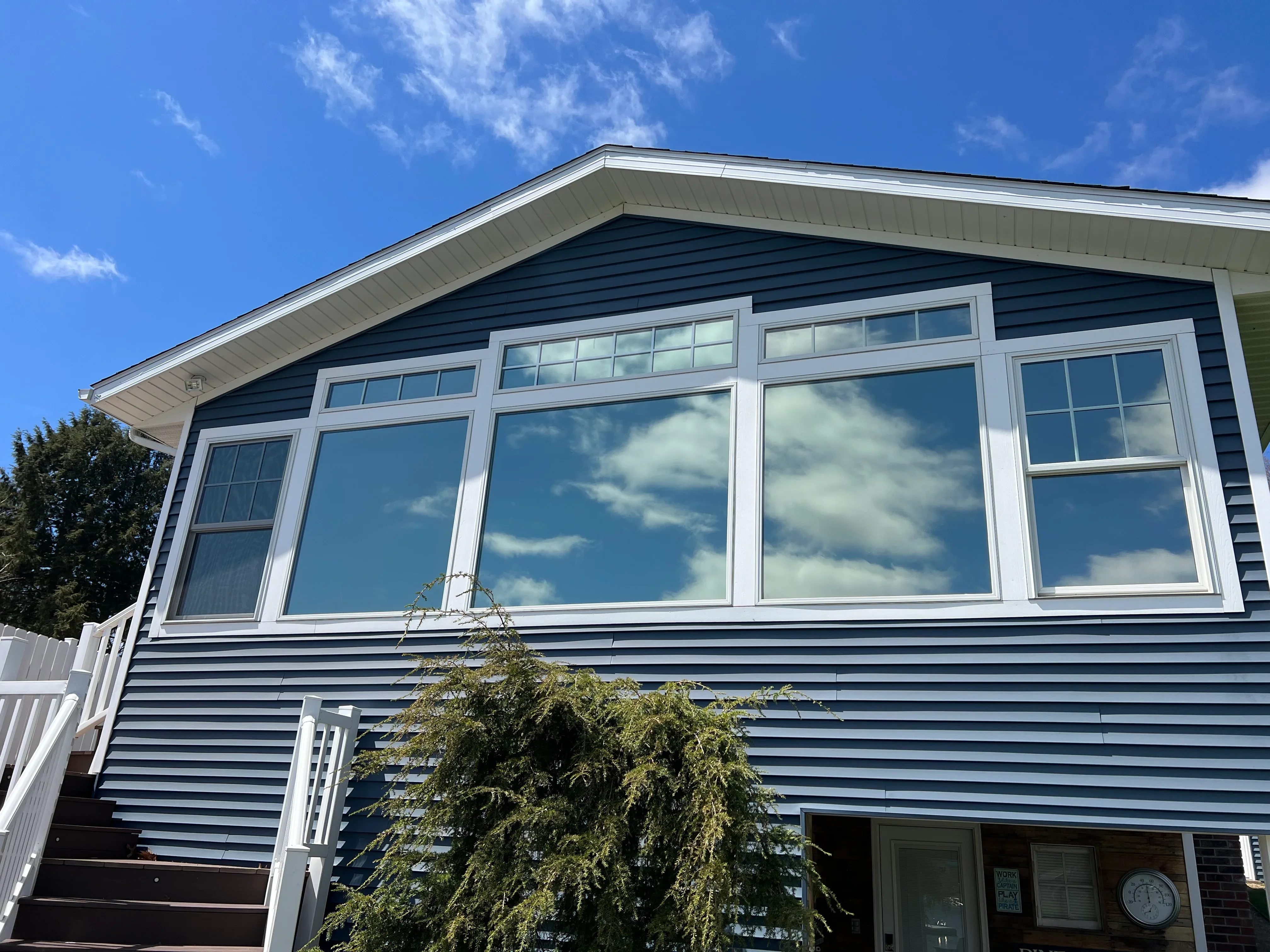 Large residential windows with white frames installed on blue vinyl siding home exterior