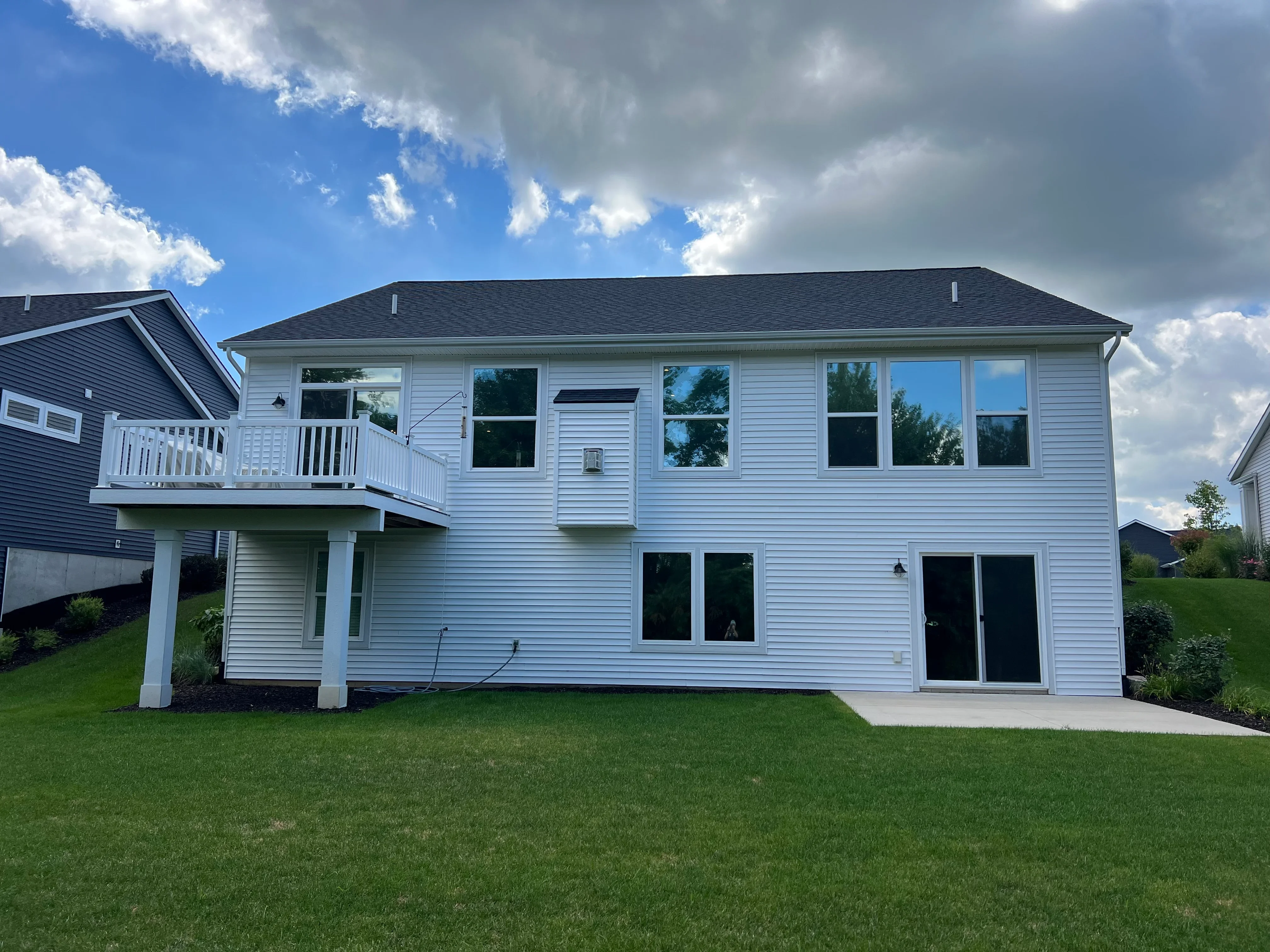 White two-story house with tinted windows on upper and lower levels, rear view with deck
