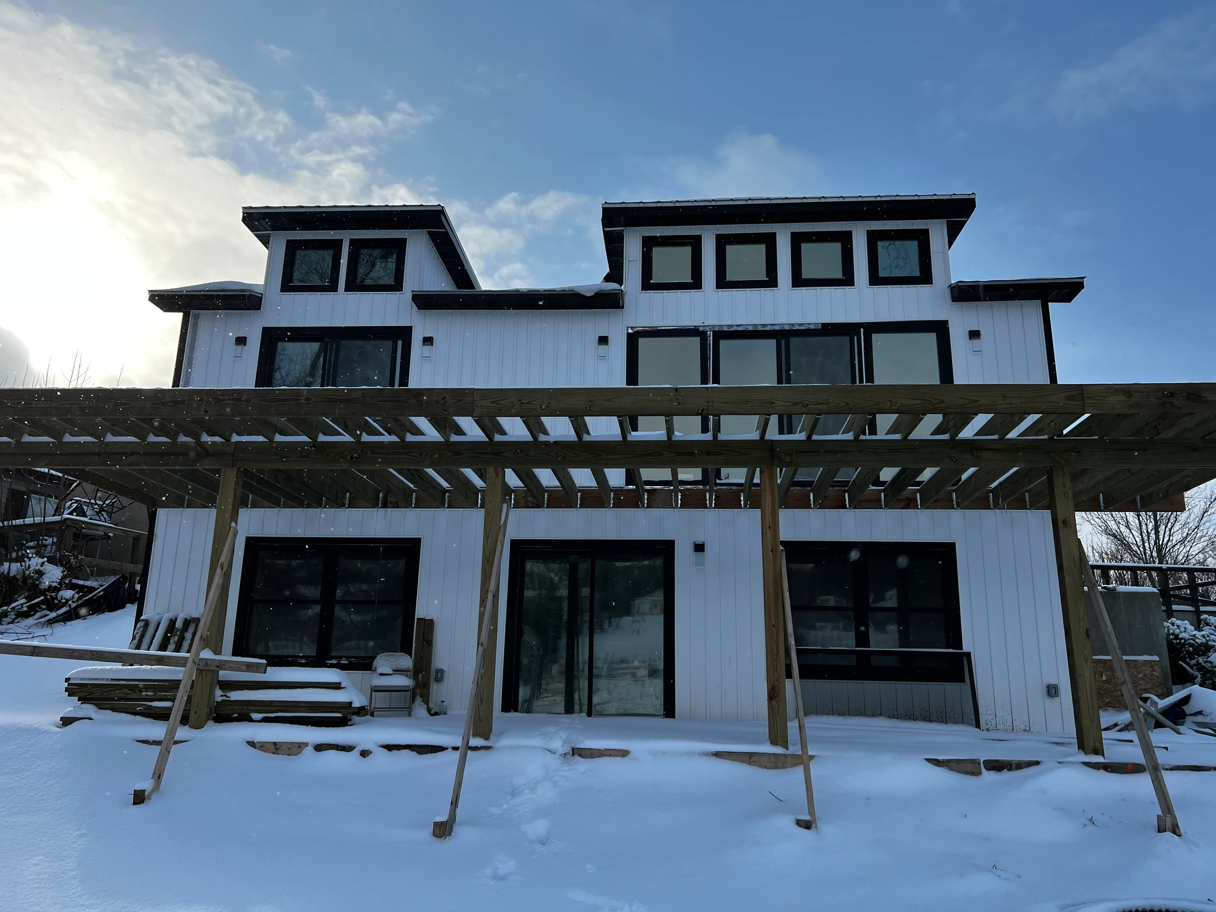 Modern home with black-framed windows and glass doors in white metal siding with wooden pergola