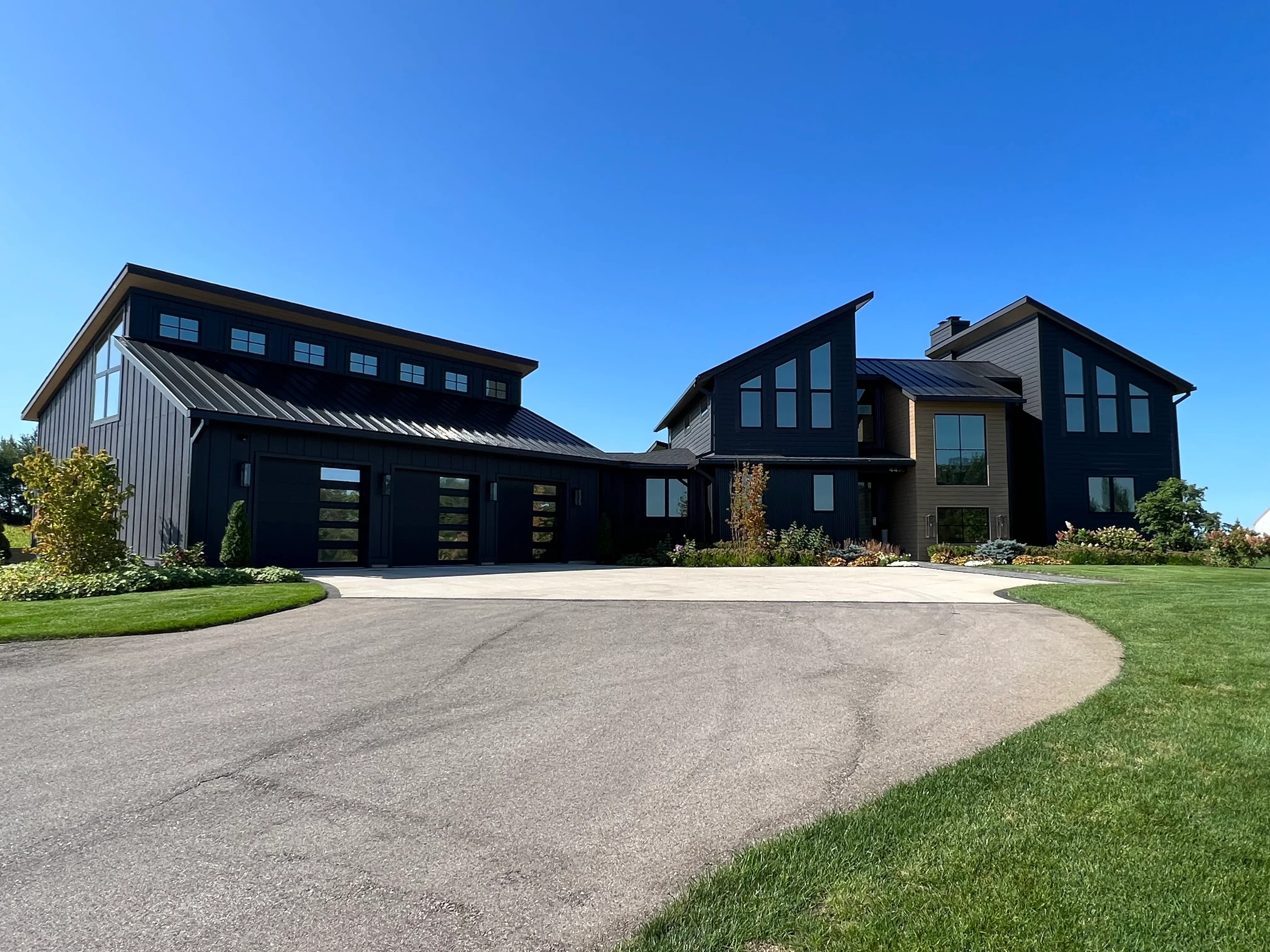 Black modern farmhouse with tinted windows and glass garage doors, metal roof accents