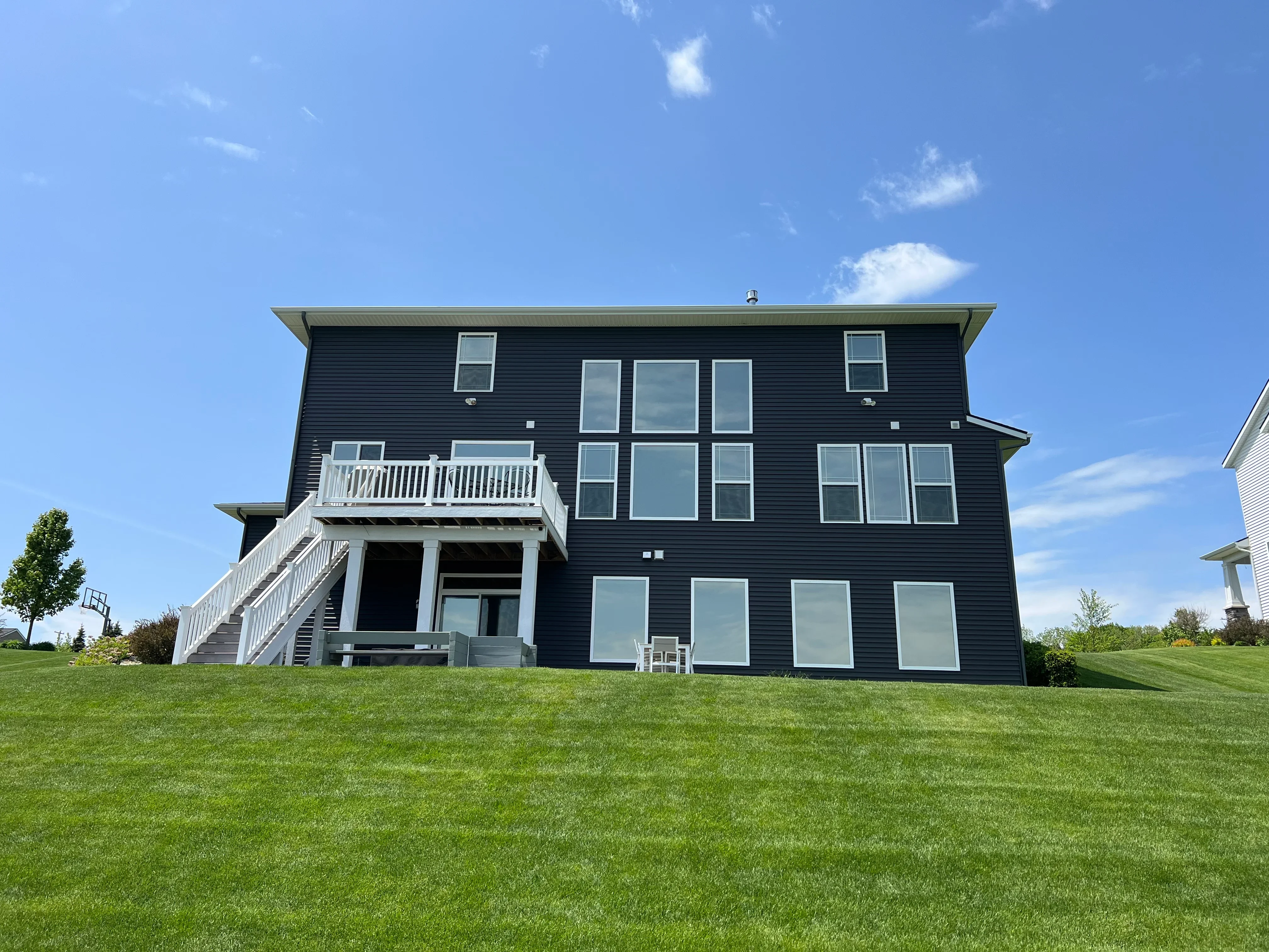 Dark-tinted windows on black vinyl-sided residential home with white deck and stairs