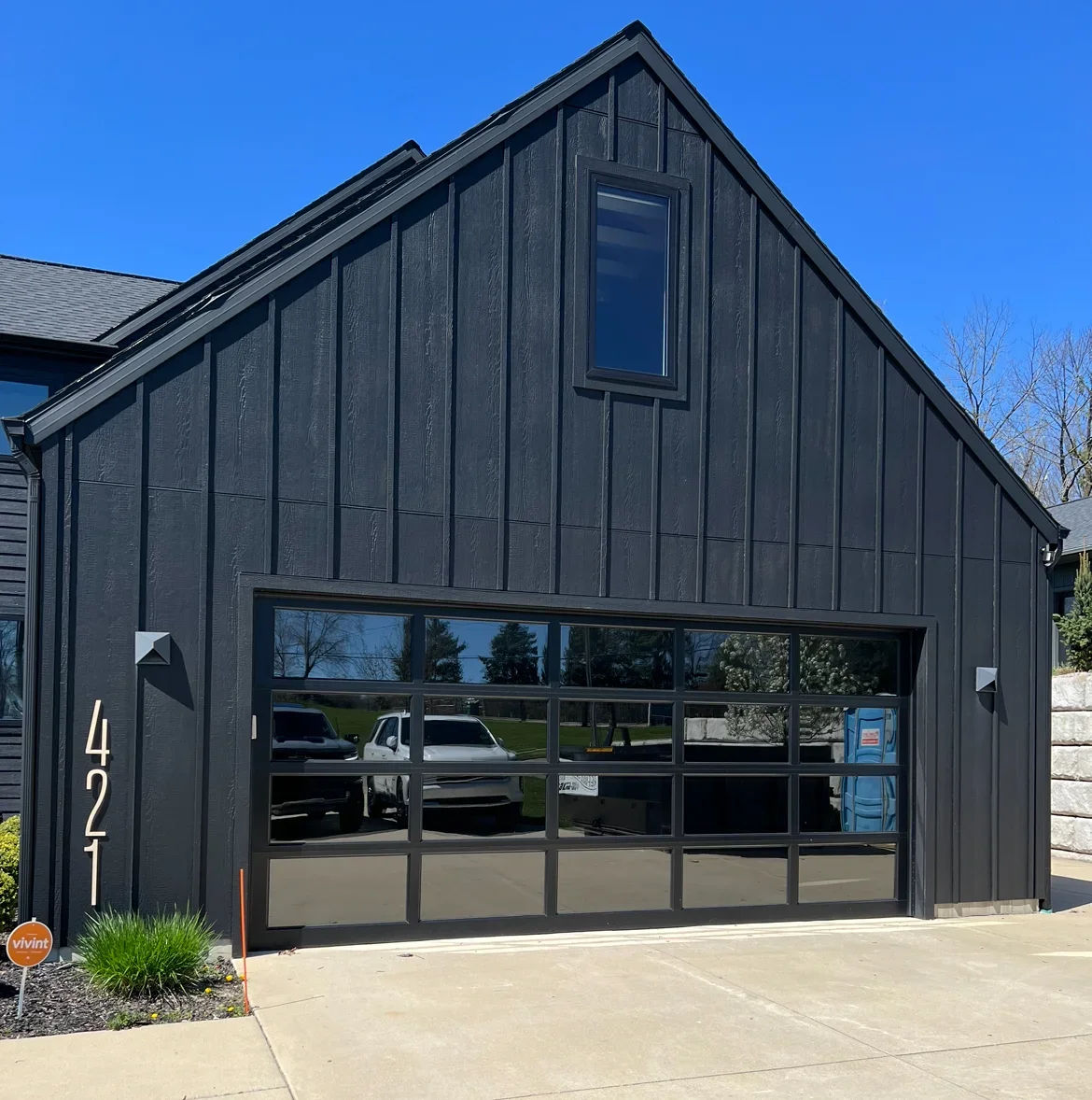 Black garage door with tinted glass panels and metal framing on modern home exterior